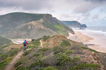 happy active senior woman cycling on the the rocky cliffs of the Vicentina coast of  Algarve, Portugal near Sagres and Vila do Bispo 