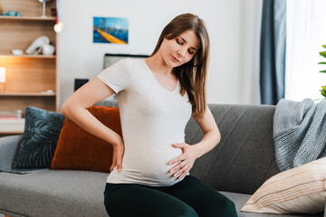 Sad pregnant woman with beautiful belly has back pain, having contractions, toned
