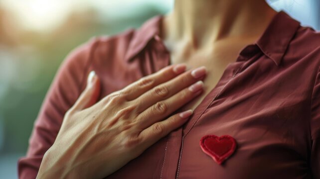 Close-up of woman with hand on chest wearing red shirt heart emblem