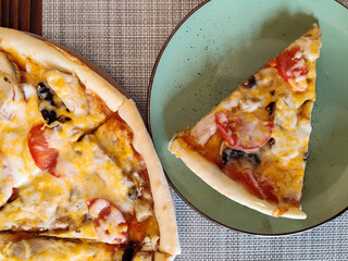 Pizza cut into portions. A piece of delicious fresh pizza on green plate, against background of gray napkin. Serving food in cafe. Top view. Close-up.