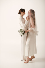 Two young women, dressed in white, embrace on their wedding day.