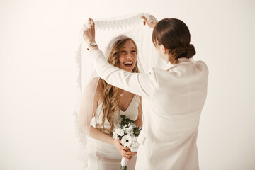 Two brides in white wedding attire share a joyful moment during their wedding ceremony, as one...