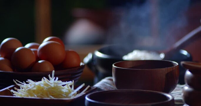 A porridge shop at night on the side of the road as the cook uses a wooden ladle to scoop porridge into a wooden bowl in a retro style. There were eggs and sliced ​​ginger placed on the table.