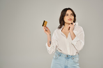 Naklejka premium Plus size woman in white shirt exudes elegance while holding a gold card against a gray backdrop.