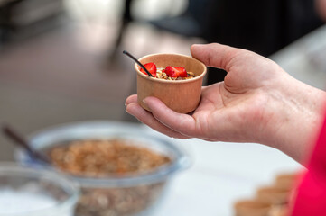 Hand holding small bowl of granola and strawberries. Background with selective focus and copy space.