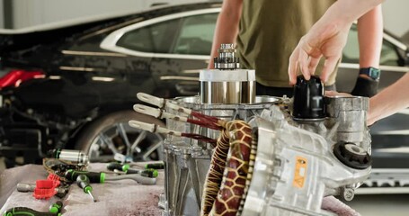 Two mechanics working on disassembled electric car engine in an auto service shop. Performing maintenance on an internal permanent magnet synchronous reluctance motor. EV repair and service concept.