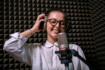 confident girl in glasses stands poised in a broadcasting studio before microphone in the acoustic chamber.