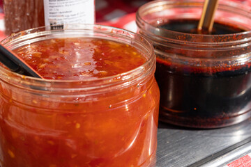 Two jars with red and dark sauces on a metal table, with spoons. Chunky, spicy red sauce and dark