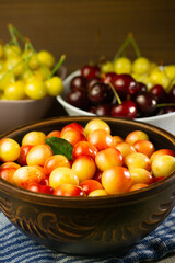 A lot of cherries of different colors in a clay plate on the table