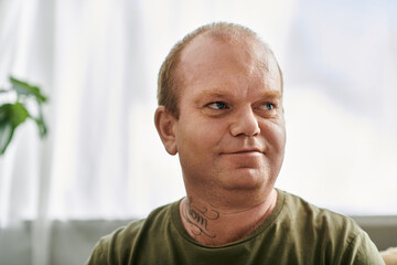 A man with inclusivity in casual attire sits at home, looking thoughtfully off-camera.