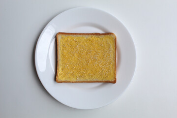 One slice of white square bread, with margarine spread and white crystal sugar topping, isolated on white background, flat lay or top view