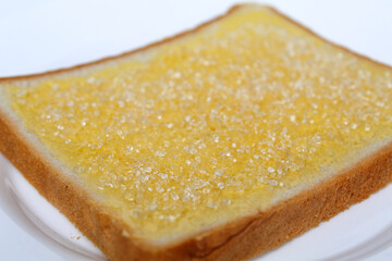 One slice of white square bread, with margarine spread and white crystal sugar topping, isolated on white background