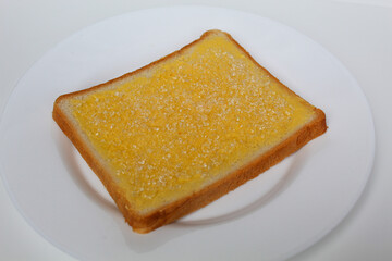 One slice of white square bread, with margarine spread and white crystal sugar topping, isolated on white background