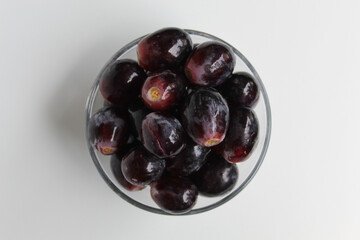 Dark purple or black grapes, off the stem, or without stalk, inside transparent bowl, isolated on white background, flat lay or top view