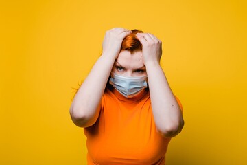 Portrait of a tired, scared woman in face medical mask, bright yellow background, coronavirus...