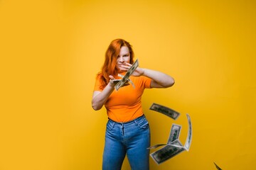 Portrait of a happy young woman, throwing banknotes, one after another, bright yellow background,...