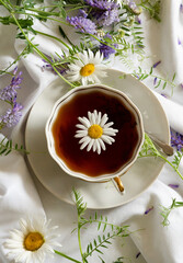 Herbal chamomile tea and chamomile flowers near teapot and tea glass. Rural or countryside background.
