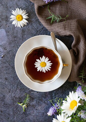 Herbal chamomile tea and chamomile flowers near teapot and tea glass. Rural or countryside background.