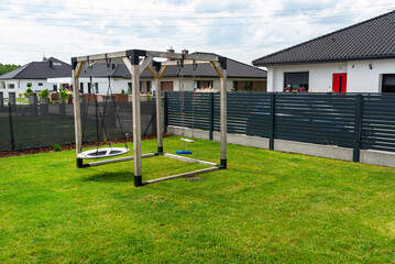 A modern, square-shaped wooden playground, made of metal corners, standing on the lawn in the yard.