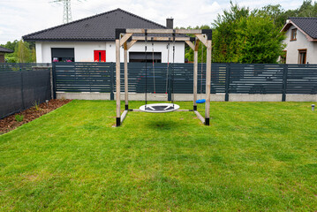 A modern, square-shaped wooden playground, made of metal corners, standing on the lawn in the yard.