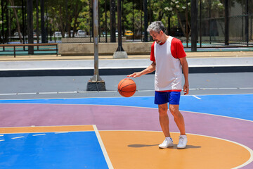 Senior Asian man in retirement age is playing basketball at outdoor court for healthy and fun activity to exercise and workout against aging illness