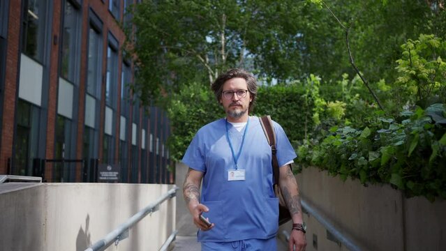 Video of handsome doctor in uniform outdoors, scrolling phone. Work-life balance of healthcare worker.
