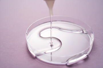 Serum or cosmetic oil flows into a transparent bowl on a purple background.