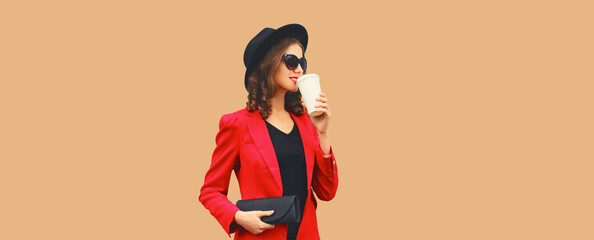 Stylish elegant woman posing in business suit, red blazer jacket, black hat with handbag looks away