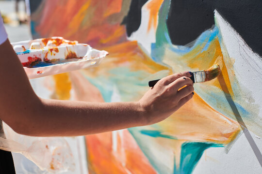 Female painter hand passionately paints picture with paintbrush for outdoor street exhibition using vibrant colors, close up view