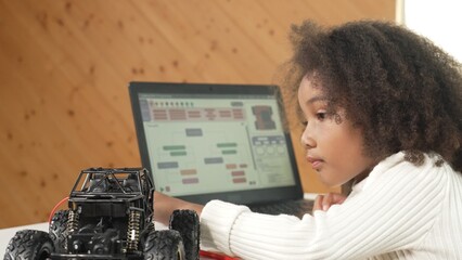 Smart african girl build robotic car while using wires while using laptop setting or writing prompt code. Skilled female student working on computer in STEM technology online classroom. Erudition.