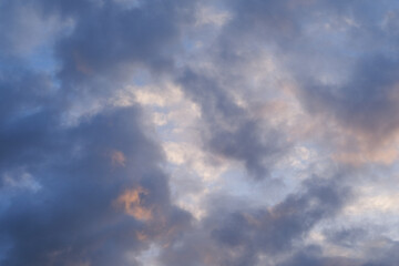 A breathtaking view of the sky during autumn evening, featuring dramatic clouds bathed in the soft colors of the setting sun