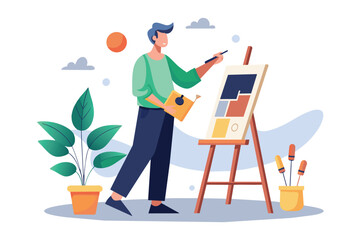Fototapeta premium A man in green shirt and black pants paints a colorful design on a canvas using a paintbrush. He holds a yellow book in his left hand.