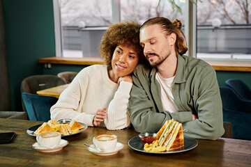 An African American woman and a man are seated at a table, sharing a meal in a modern cafe setting.
