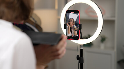 Back view influencer shoot live with smartphpone streaming using vlog video review makeup prim...