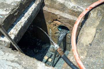 Obraz premium Sewer pipe cleaning in a private house. Mud and sludge remover in clean hole in drainage pipe underground with water - splashing water hose in hole.