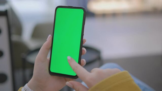 Hand holding smartphone with green screen, perfect for mockups or chroma key effects, blurred outdoor setting.