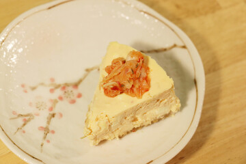 Food(dessert)-there is a piece of cheesecake on a white plate with some orange vegetable decoration.