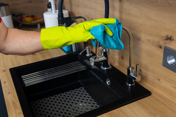A man's hand in a light green glove cleans a chrome faucet in the kitchen