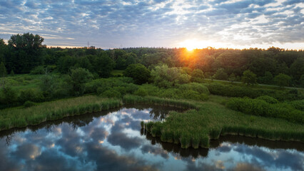 Drohnen Aufnahme des Sonnenaufganges über den Bäumen. Die Wolken spiegeln sich im Wasser eines...