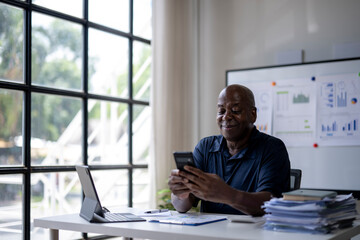 A man is sitting at a desk with a laptop and a cell phone