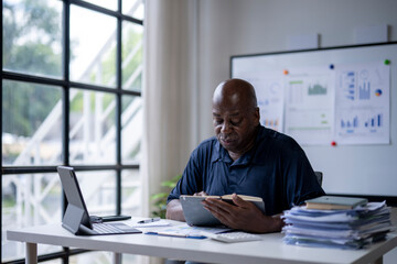 A man is sitting at a desk with a laptop and tablet in front of him