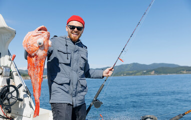 Happy Male fisherman holding red perch snapper big fish, Kamchatka Peninsula Russia. Deep sea sport...