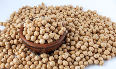A clay bowl full of chickpeas stands in a pile of scattered chickpeas. Heap of chickpeas on a white background.