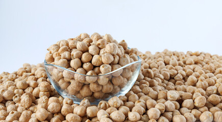 A glass bowl full of chickpeas stands in a pile of scattered chickpeas. Heap of chickpeas on a white background.