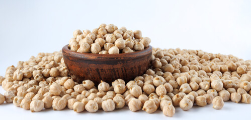 A clay bowl full of chickpeas stands in a pile of scattered chickpeas. Heap of chickpeas on a white background.