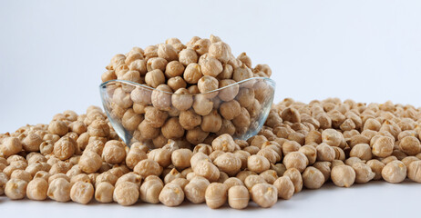 A glass bowl full of chickpeas stands in a pile of scattered chickpeas. Heap of chickpeas on a white background.