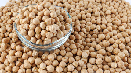 A glass bowl full of chickpeas stands in a pile of scattered chickpeas. Heap of chickpeas on a white background.
