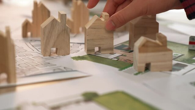 Architect and engineer discuss about building blueprint on table with architectural document, measurement tools scatter around at office, use wooden block for house positioning. Closeup. Delineation.