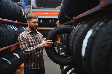 Male mechanic holding car tire in automobile store