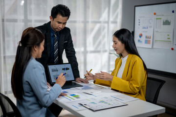 Three people are sitting at a table with a laptop and papers in front of them